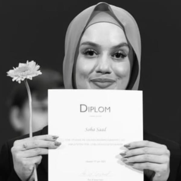 Smiling woman wearing headscarf holds a diploma certificate and a flower